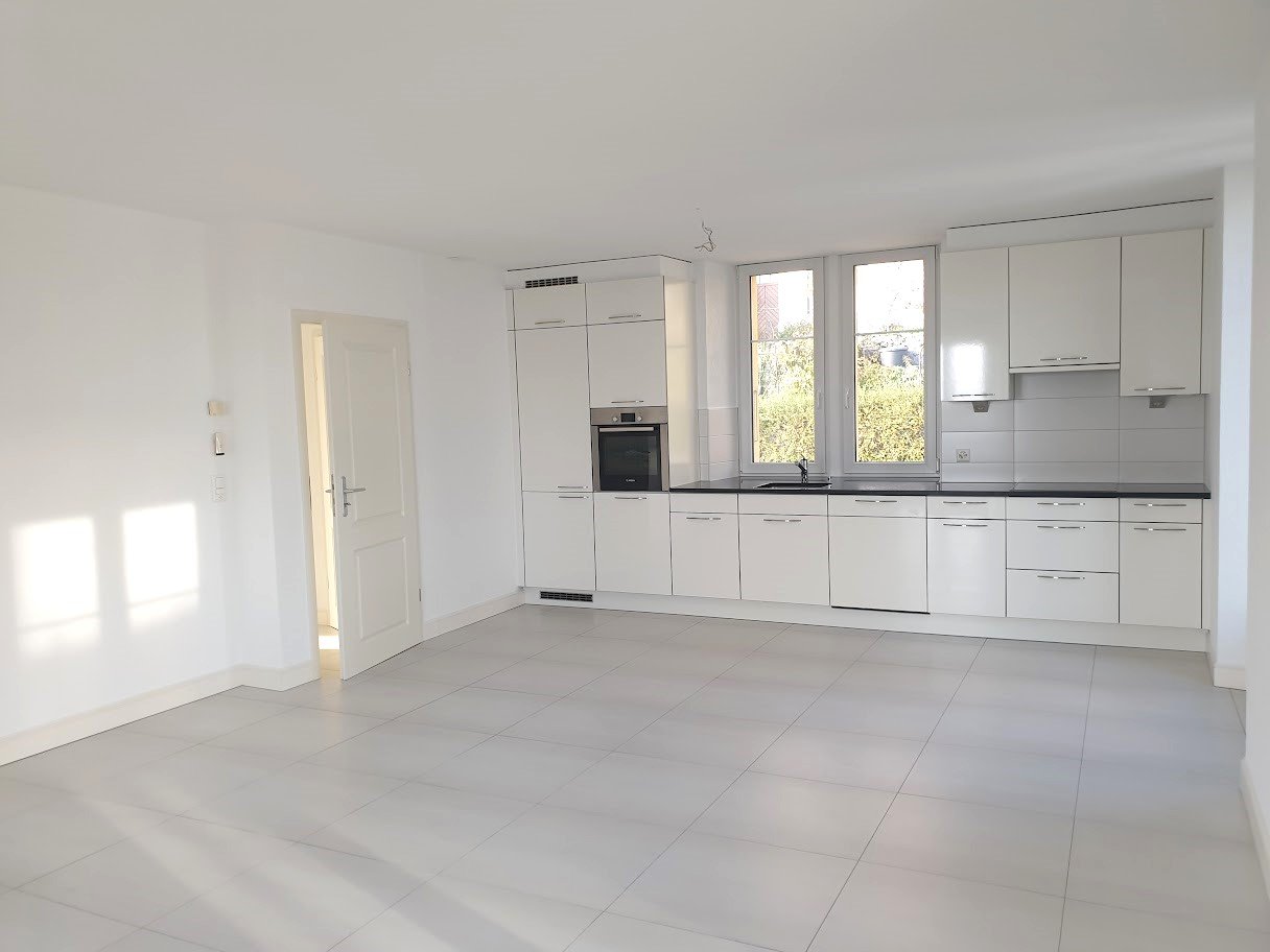 Spacious open-plan kitchen with modern white cabinets, built-in appliances including a dishwasher, and large windows providing natural light.