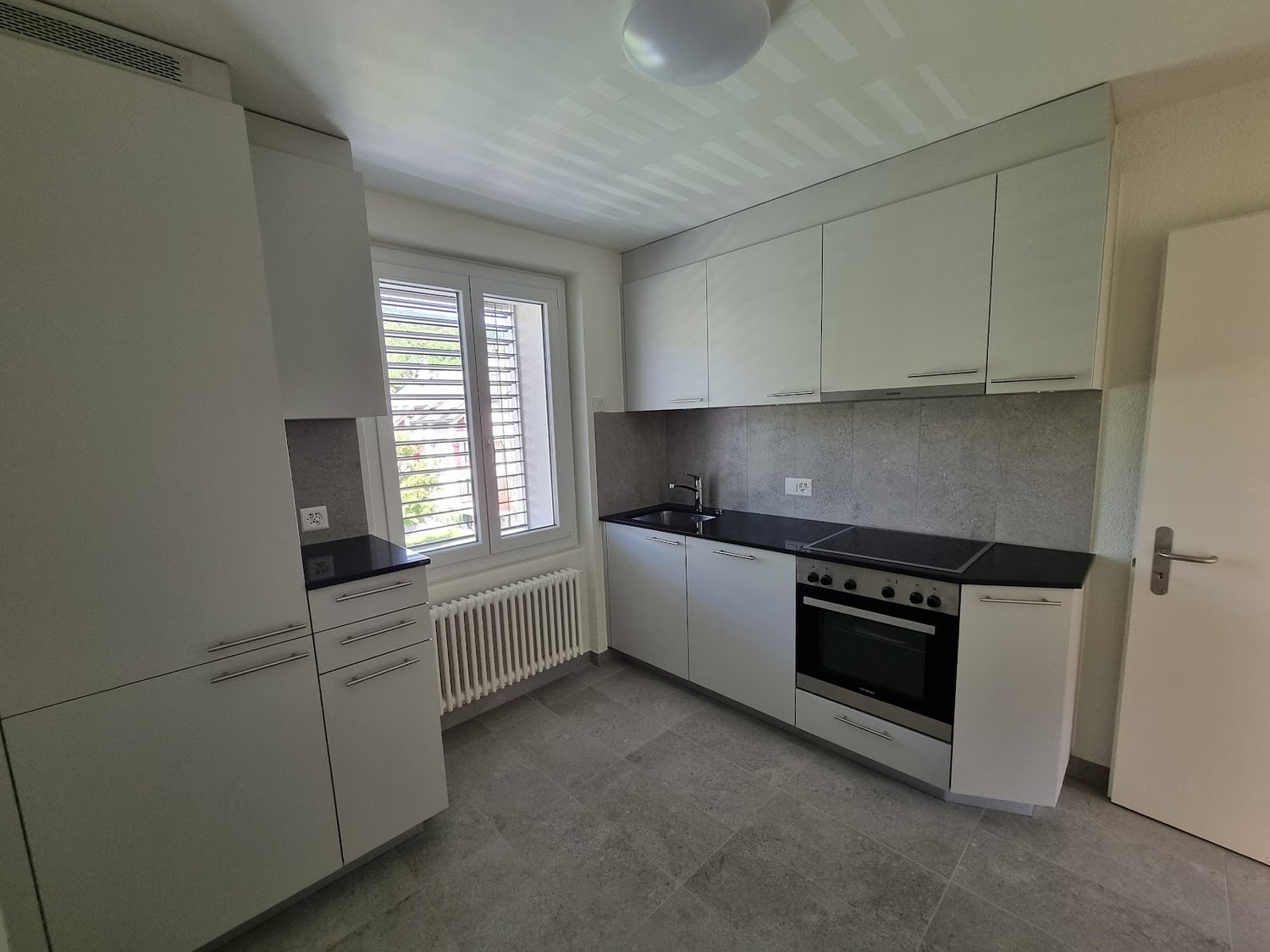 empty kitchen with white cabinets, grey tile flooring, black countertops, stainless steel sink, electric oven
