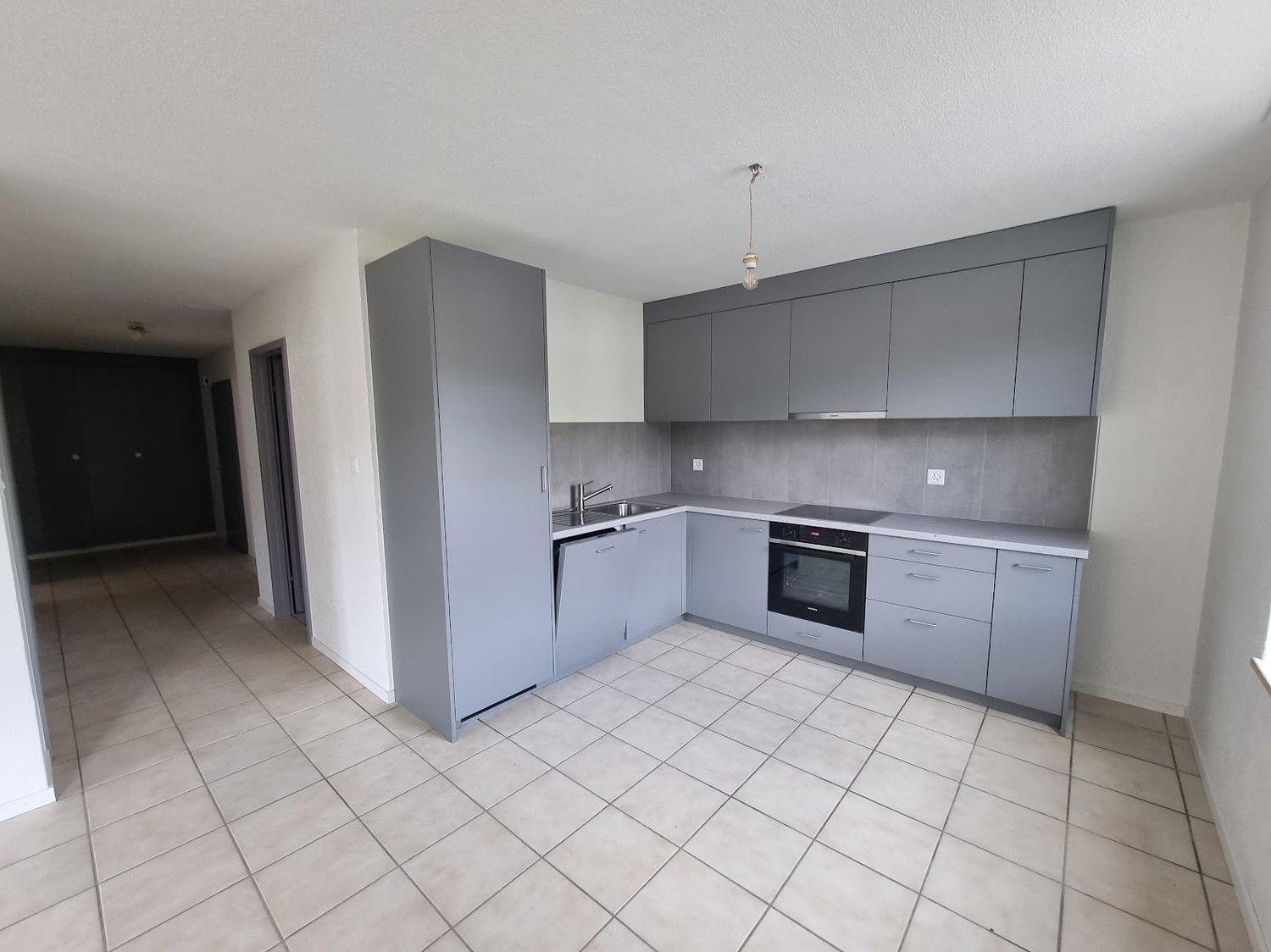 Modern kitchen with grey cabinets, built-in oven, and tile flooring. The kitchen has an open layout and is connected to the living area.
