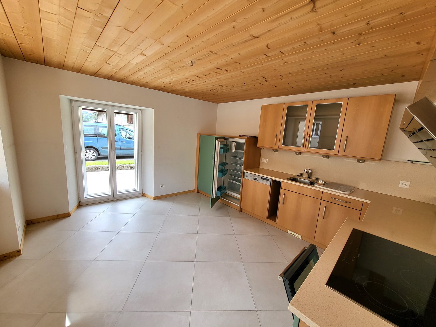 Open kitchen with wooden cabinets, tile flooring, and a sliding glass door leading to the exterior. The kitchen appears to have a dishwasher installed.