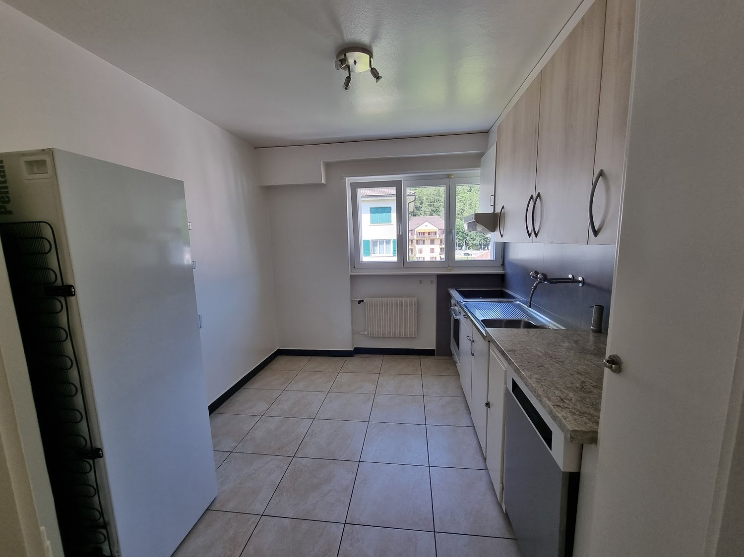 White walls, tiled floor, white cabinets, granite countertop, stainless steel sink, dishwasher, white refrigerator, radiator, window