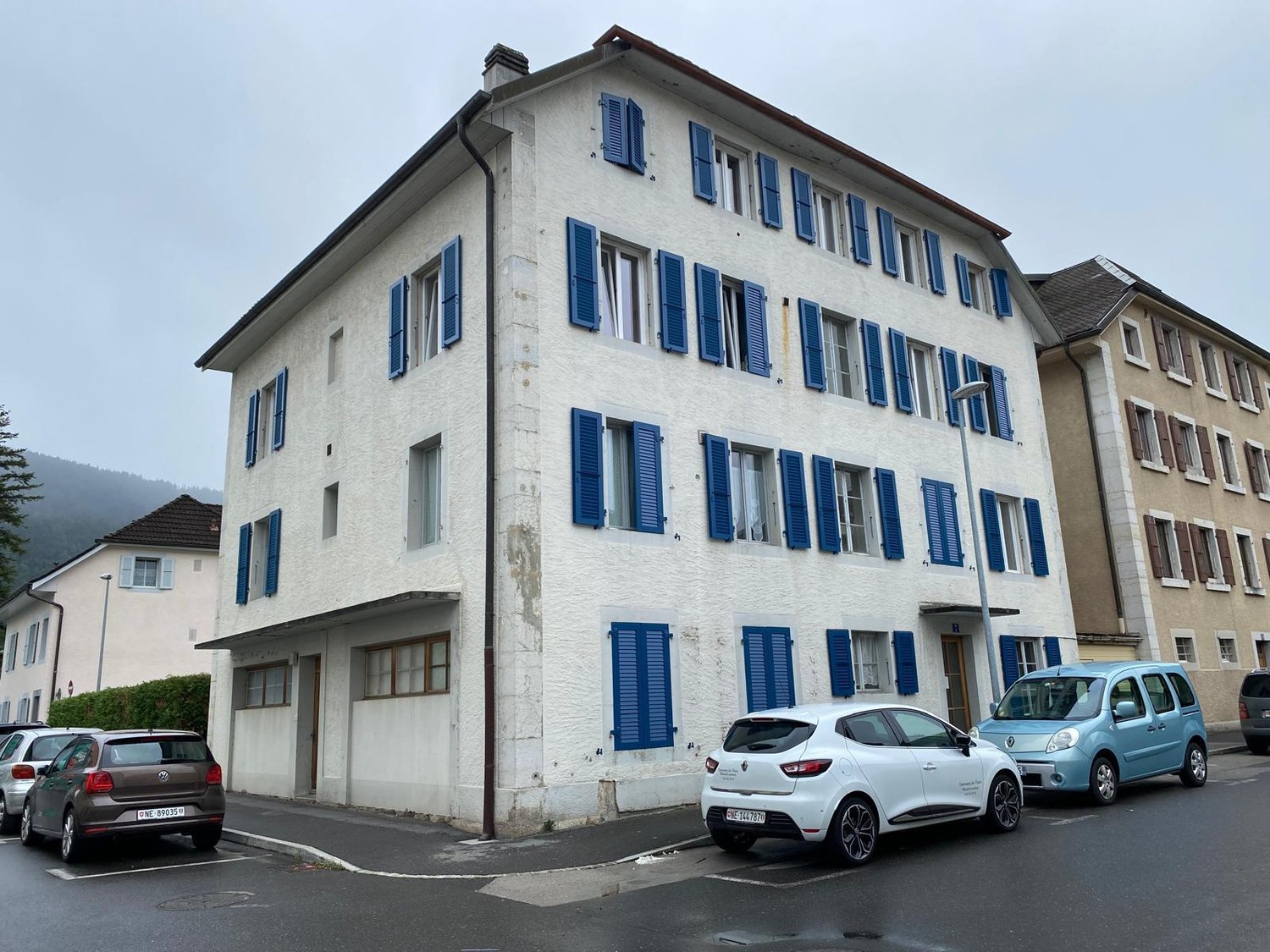 multistory residential building with many windows, blue shutters, streetlight, and parking