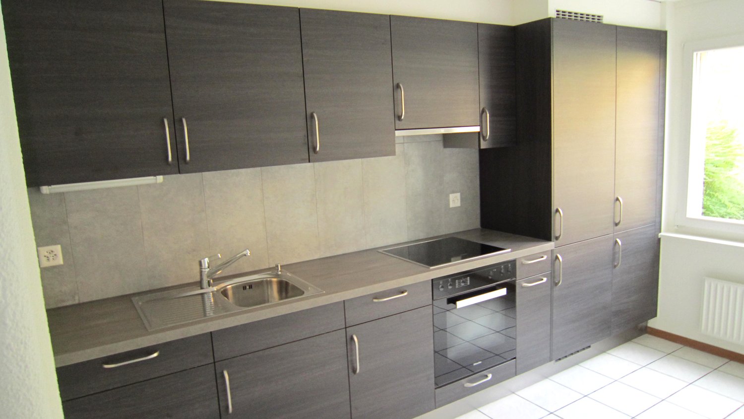 gray cabinets, stainless steel sink, black countertop, gas stove, electric oven, power outlet, faucet, window