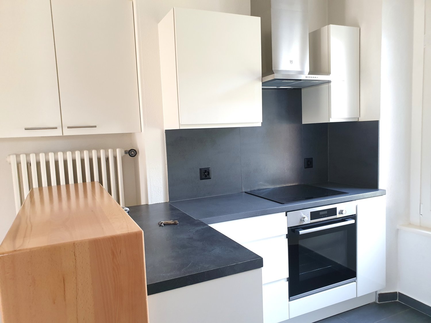 modern kitchen, dark countertops, wooden island, gas stove, oven, white cabinets, exhaust hood, large windows