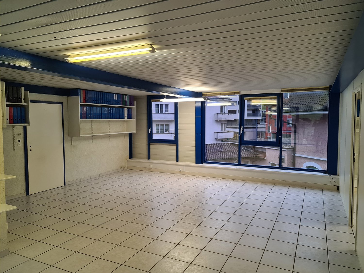 Empty room with large windows, white tile flooring, built-in shelves, and bright lighting