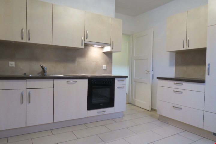 Modern kitchen with white cabinets, tiled floor, built-in oven, sink, faucet, black countertop, power outlet on the wall