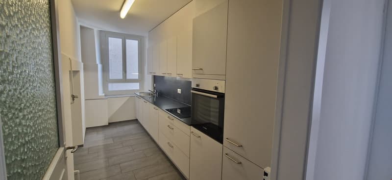 modern kitchen, white cabinets, tiled floor, black countertops, built-in oven, sink, dishwasher, washing machine