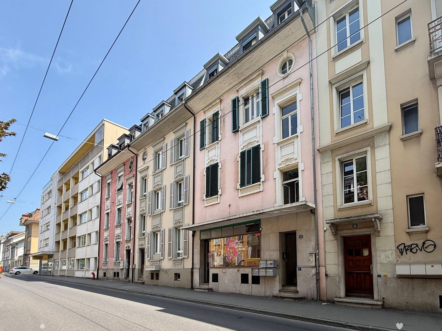 An outdoor view of a row of buildings with windows and doors on a street with parked cars, street lights, and wires