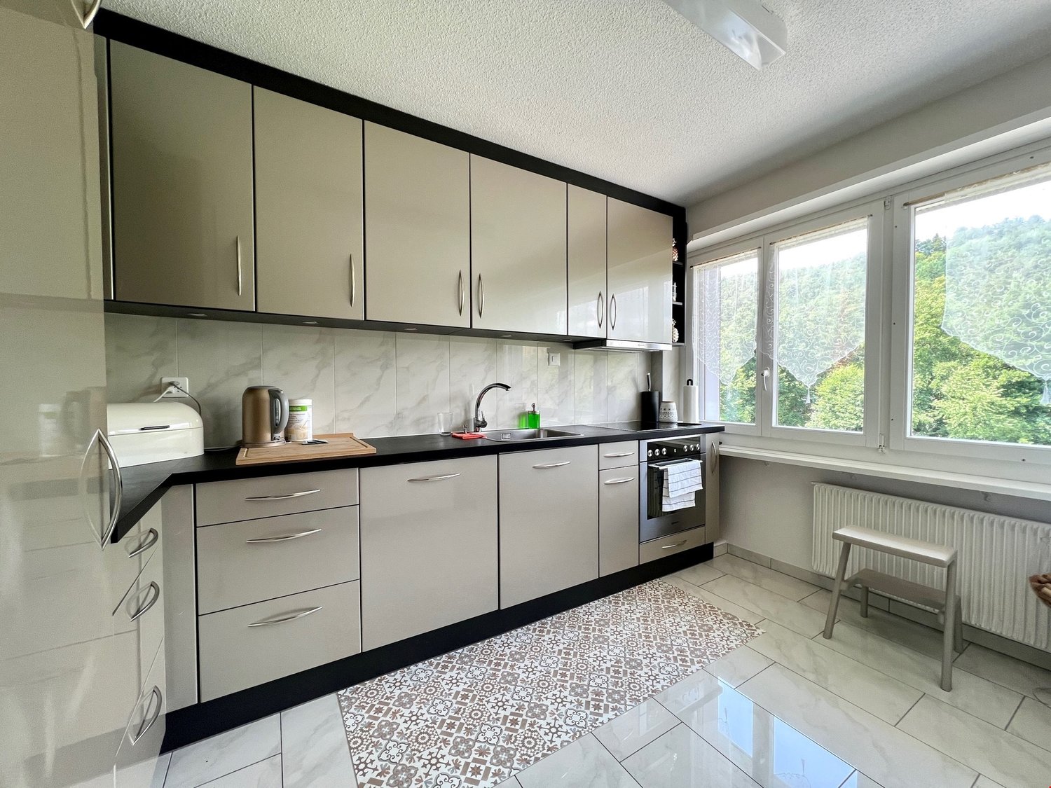 modern, grey cabinets, black countertops, large windows, stainless steel oven, white tiles, and a white microwave