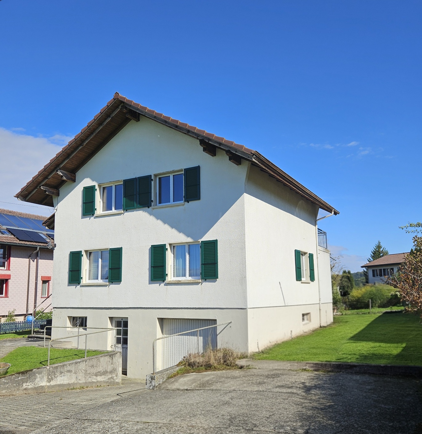 Two story white house with brown roof, multiple windows with green shutters, garage, driveway