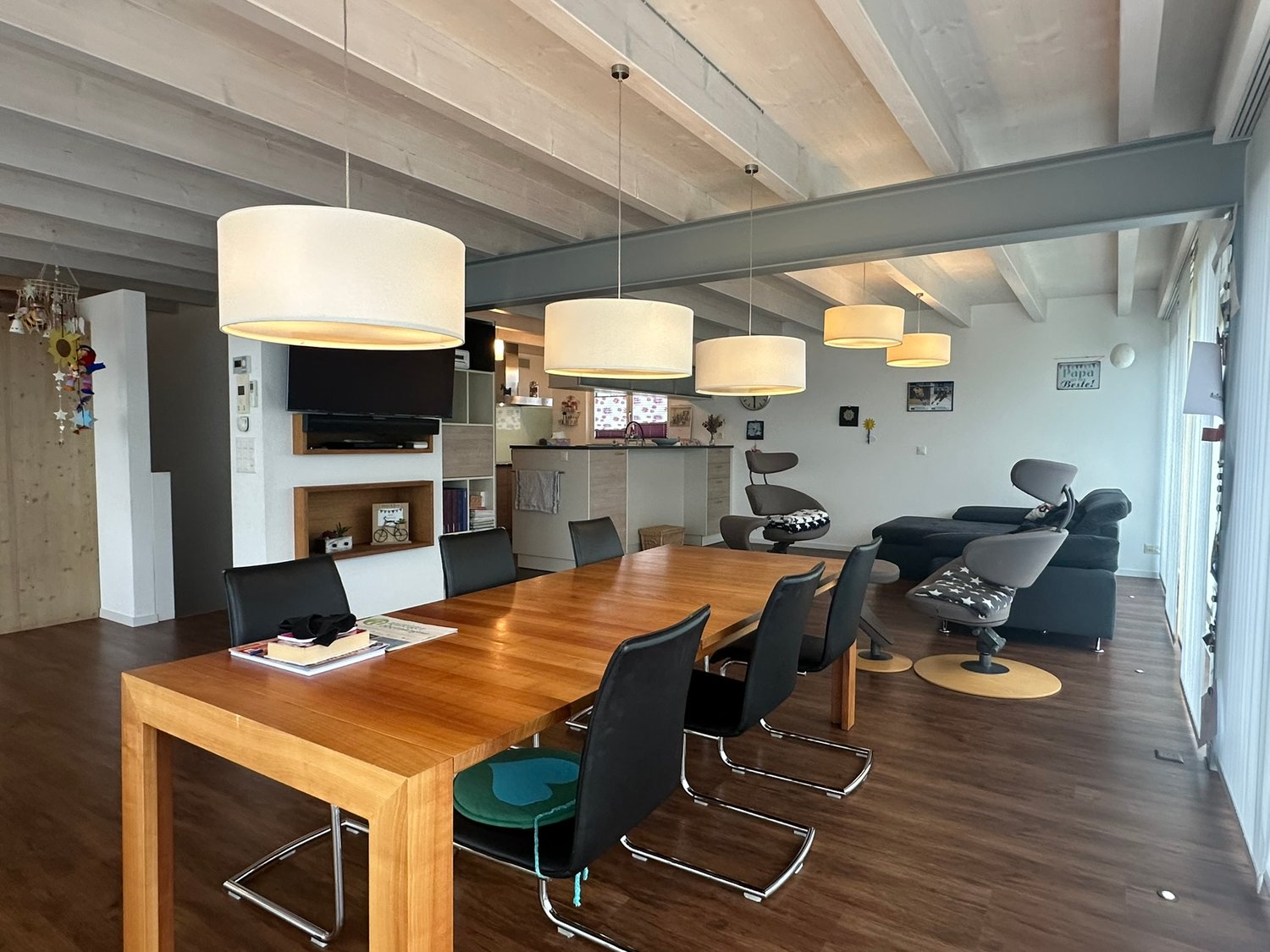 dining room, hardwood floor, large wooden table, wooden chairs, ceiling beams, hanging lamps, kitchen, TV