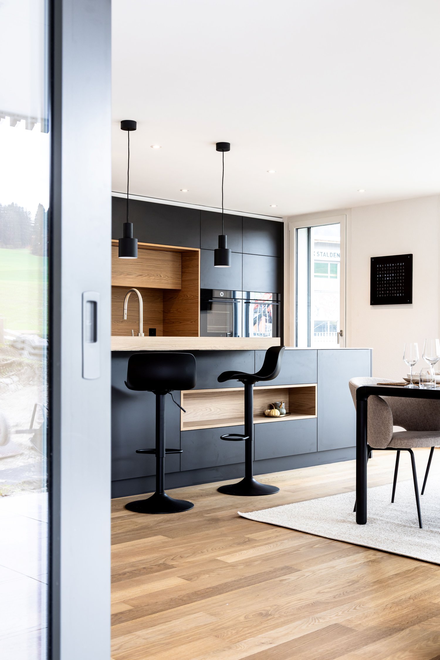 open plan kitchen and dining area, wooden floor, wooden cabinets, black barstools, white and black kitchen island, modern faucet