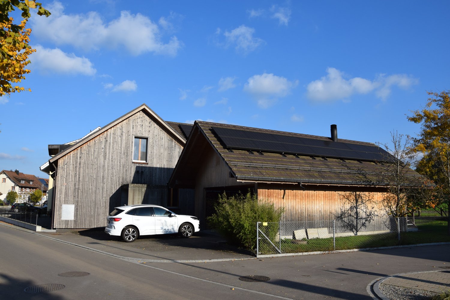 Detached house, solar panels on the roof, white car parked in front, wooden exterior, fenced yard, chimney