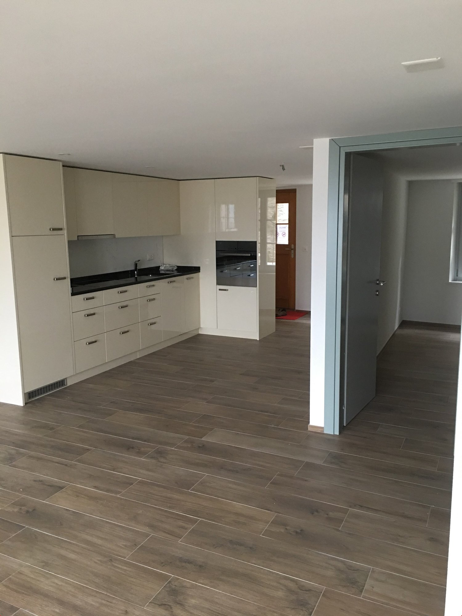 White wooden cabinets, white countertops, black floor, built-in oven, silver faucet