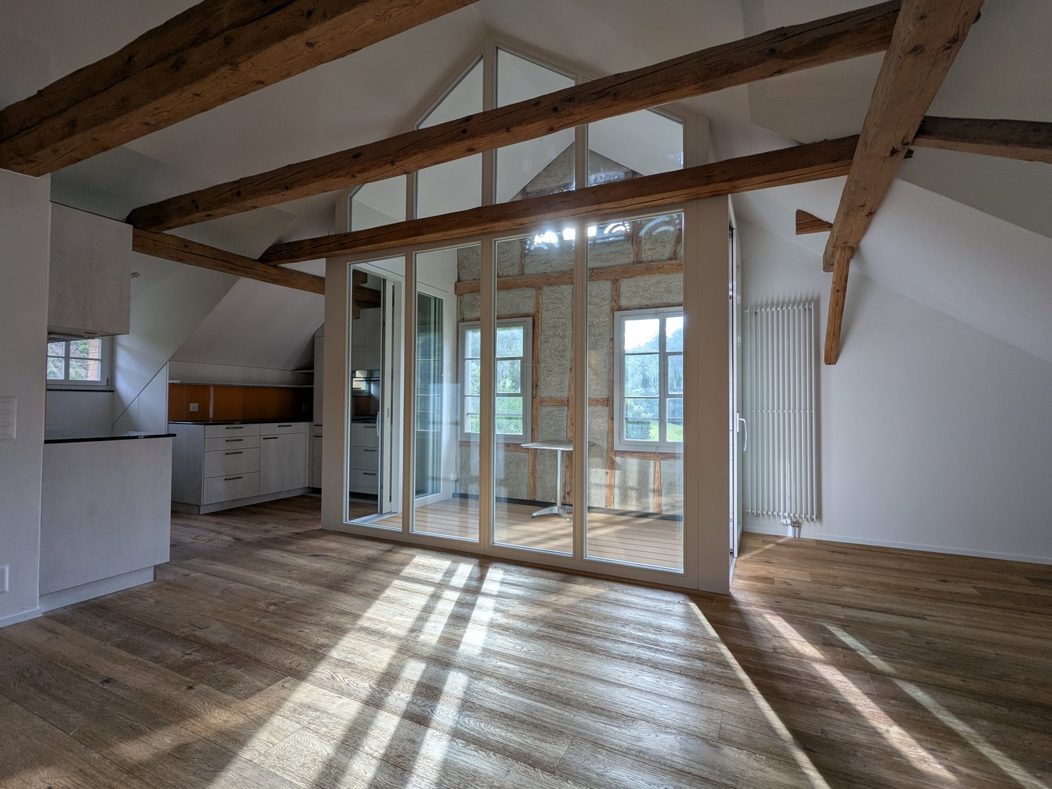 wooden ceiling beams, large windows, wooden floor, kitchen with white cupboards