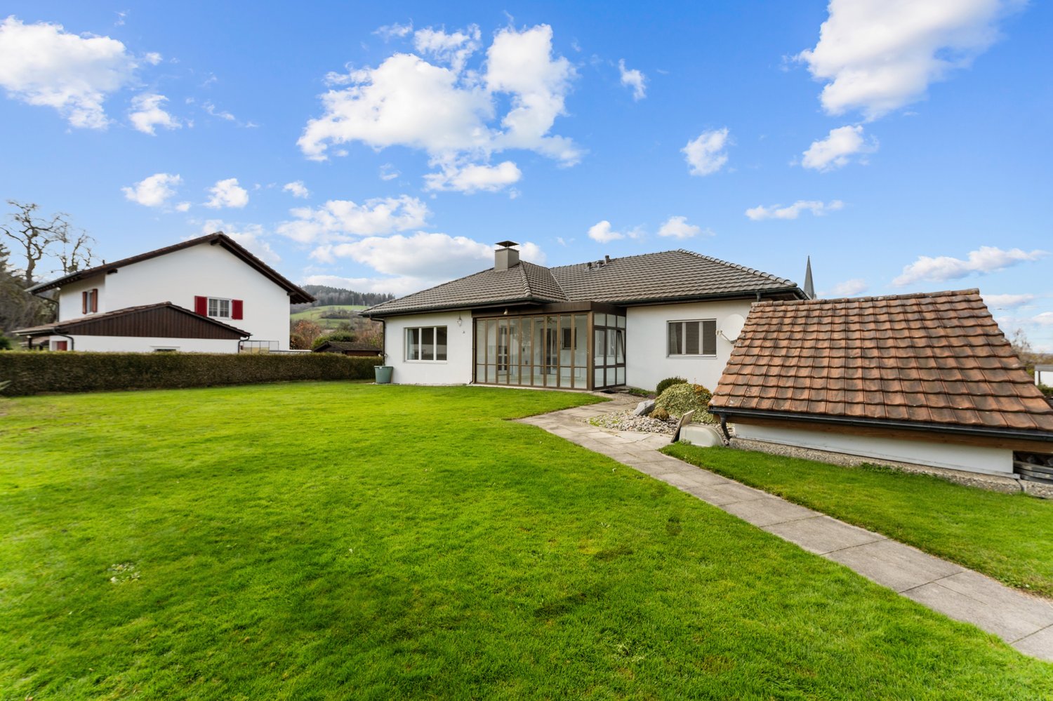 Two houses with green lawn, brown roof, garden, well-maintained green grass, pathway, bushes