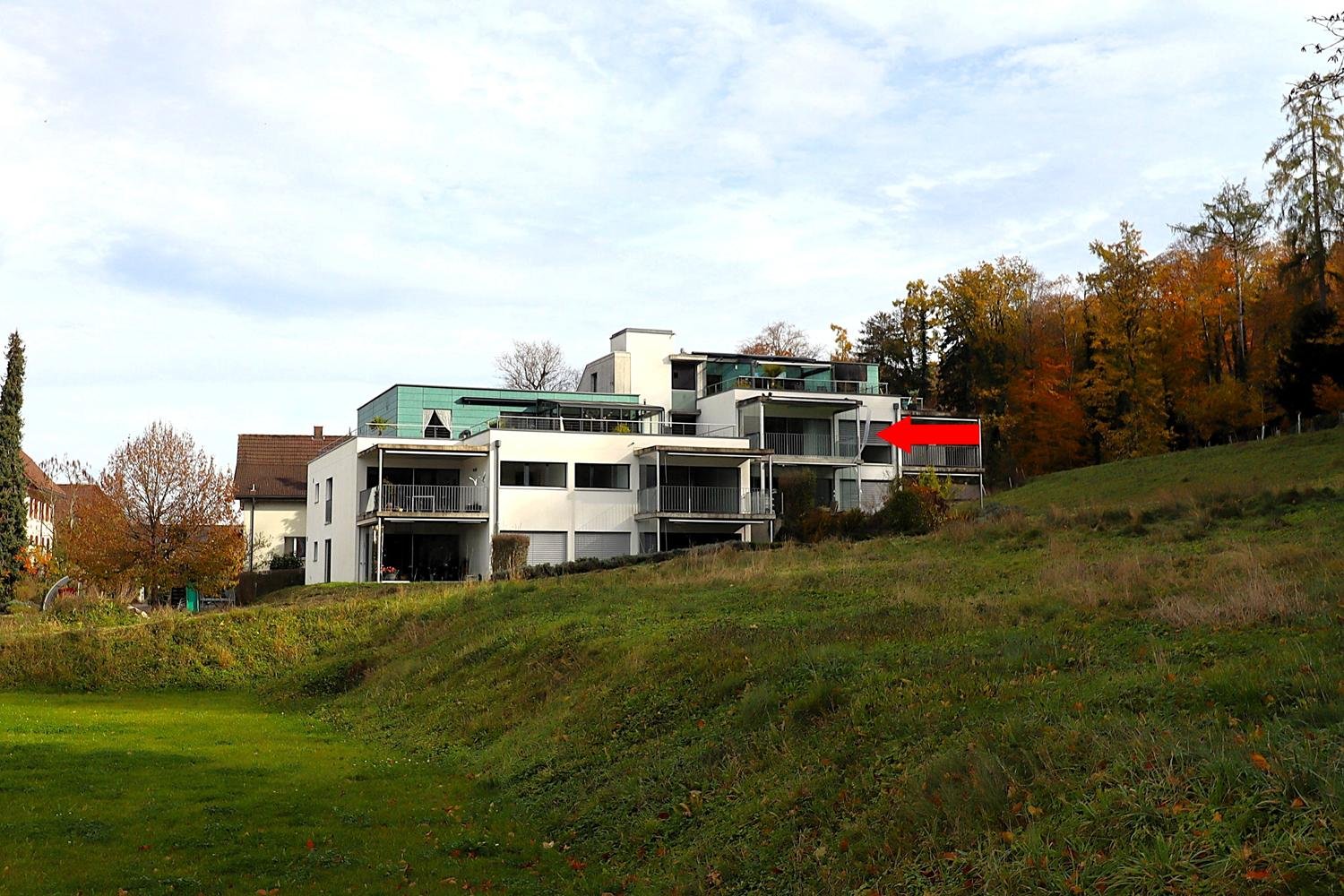 3 story building, white facade, green roof, balcony, set on a hill