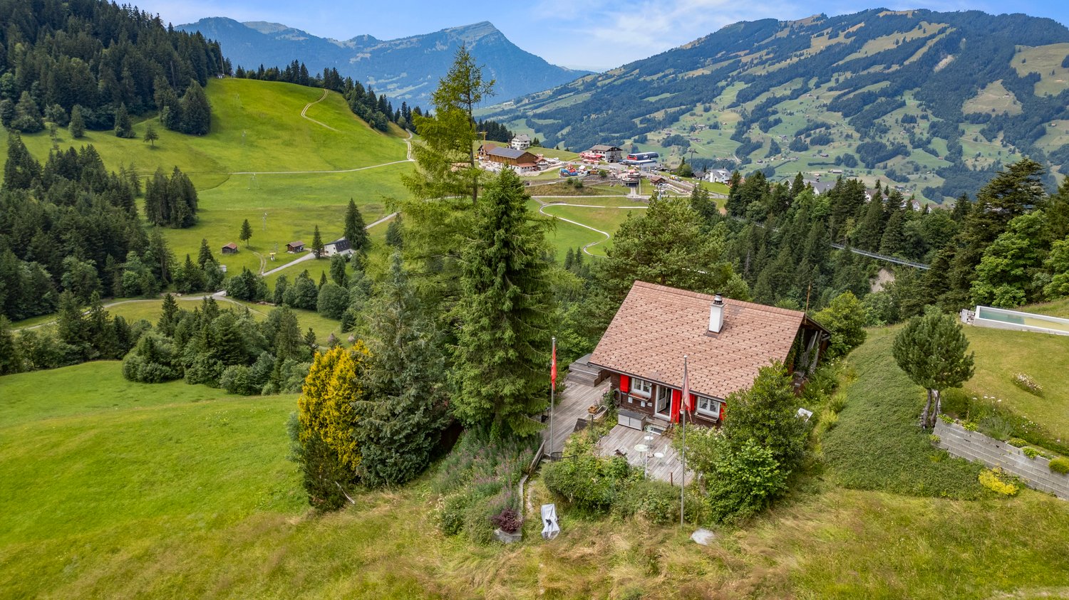 Rustic house, nestled in the Swiss Alps, with wooden exterior, red shutters, wooden deck, lush green surroundings, and panoramic mountain views.