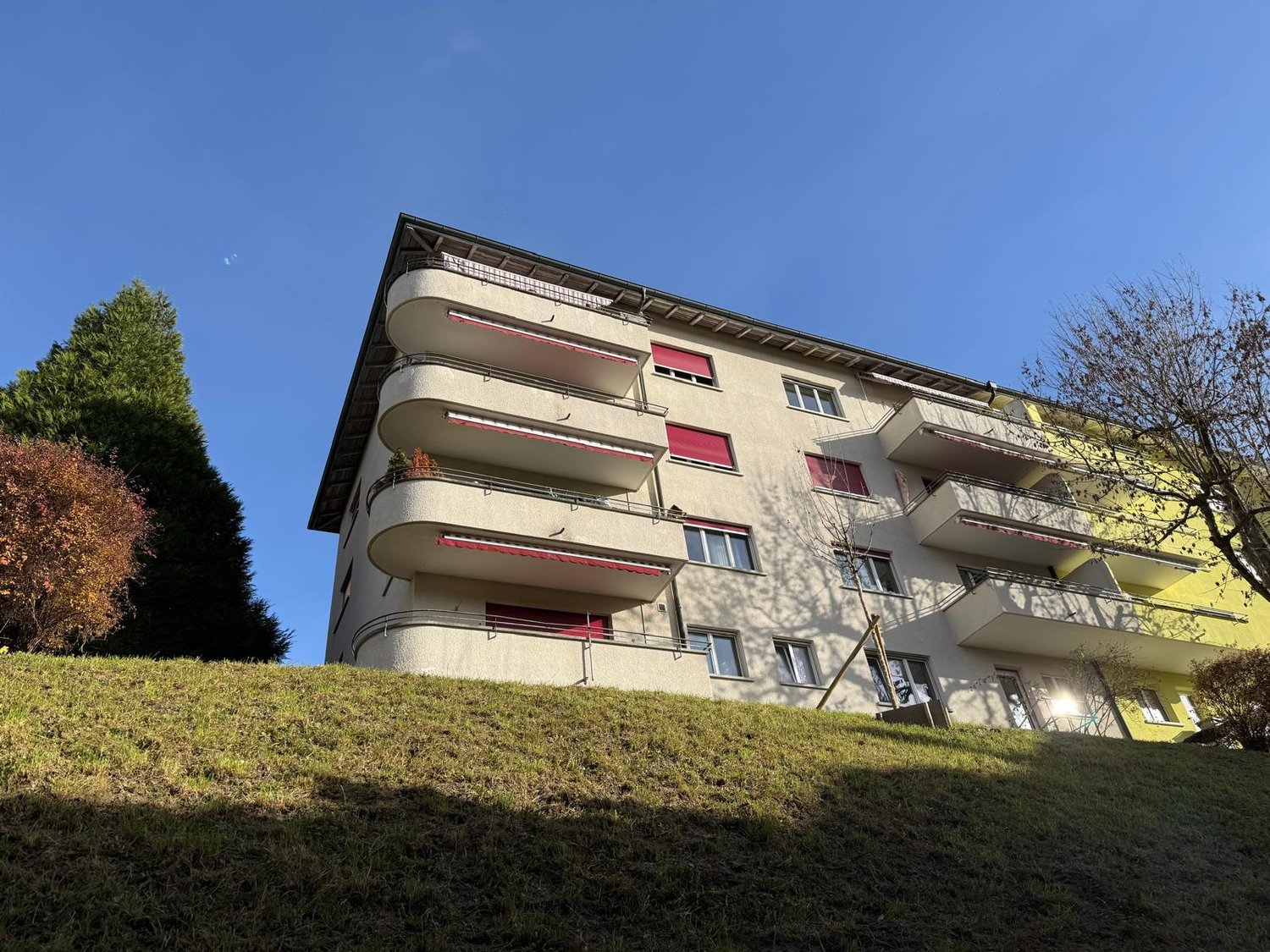 3 story building, multiple balconies, white exterior, red window shutters, situated on a hill