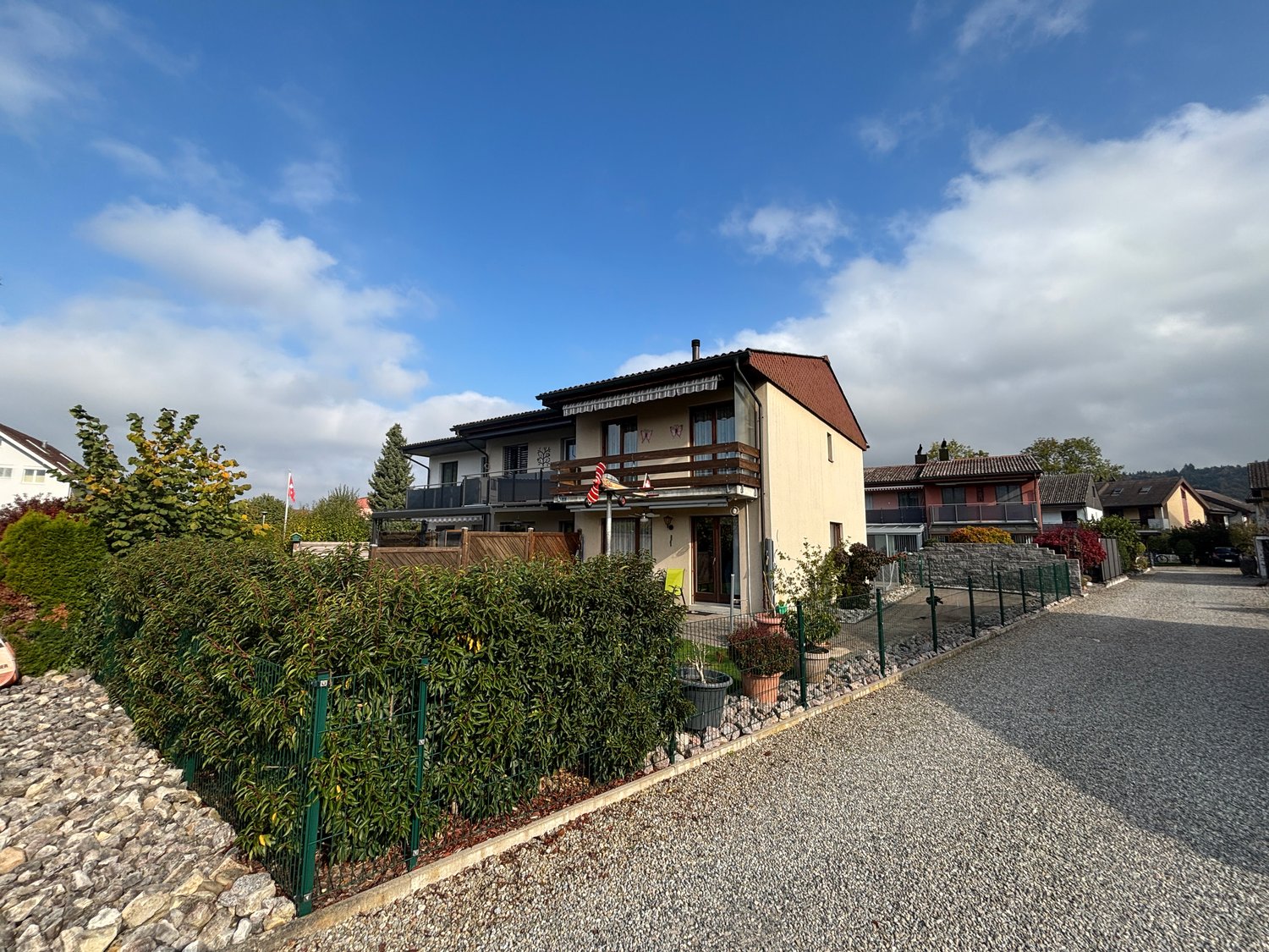 2 story house, brown roof, beige walls, multiple balconies, driveway, garden, hedges