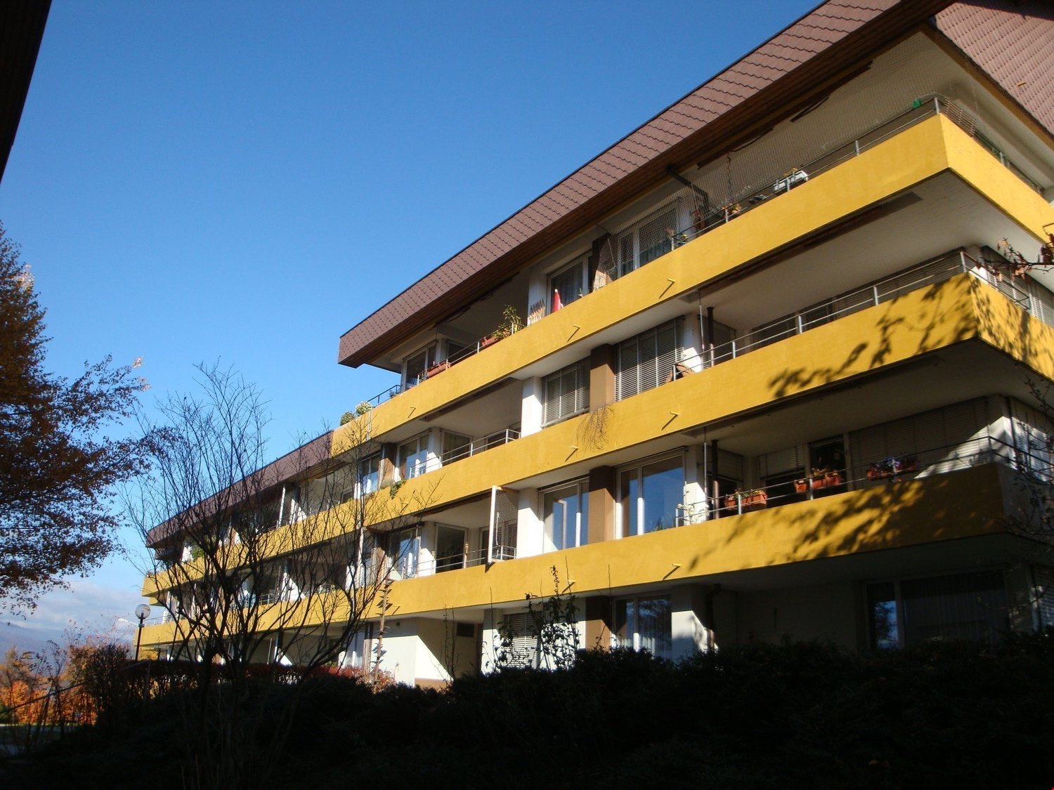 Multi-story building, yellow exterior, multiple balconies, brown roof, glass windows