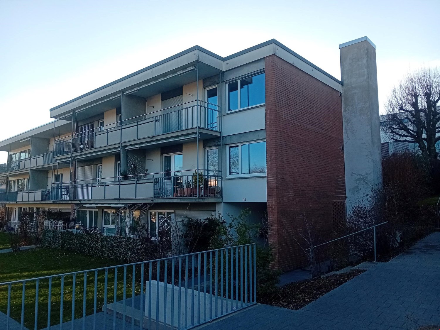 modern building, brick exterior, multiple floors, balconies, garden area, pathways, plants