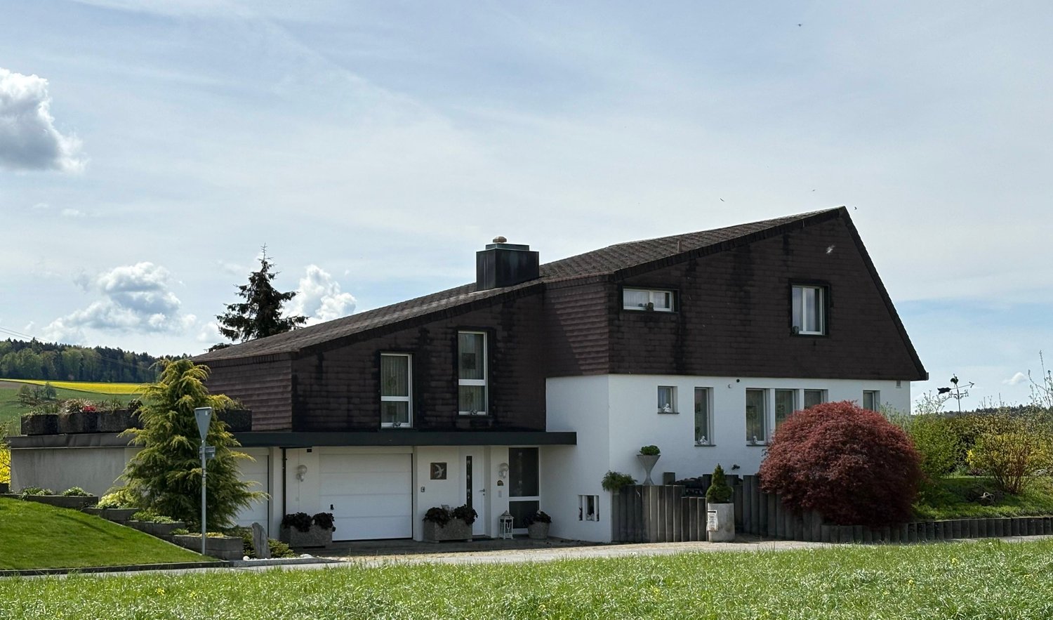 modern style house, brown roof, white walls, garage, double-fronted, 3 stories, several windows, surrounded by greenery