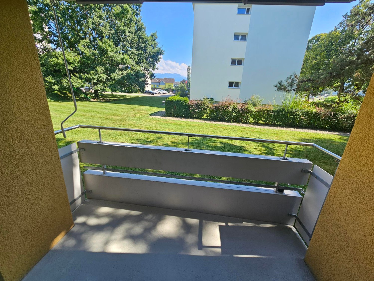 A balcony overlooking a well-maintained garden and green grassy field.