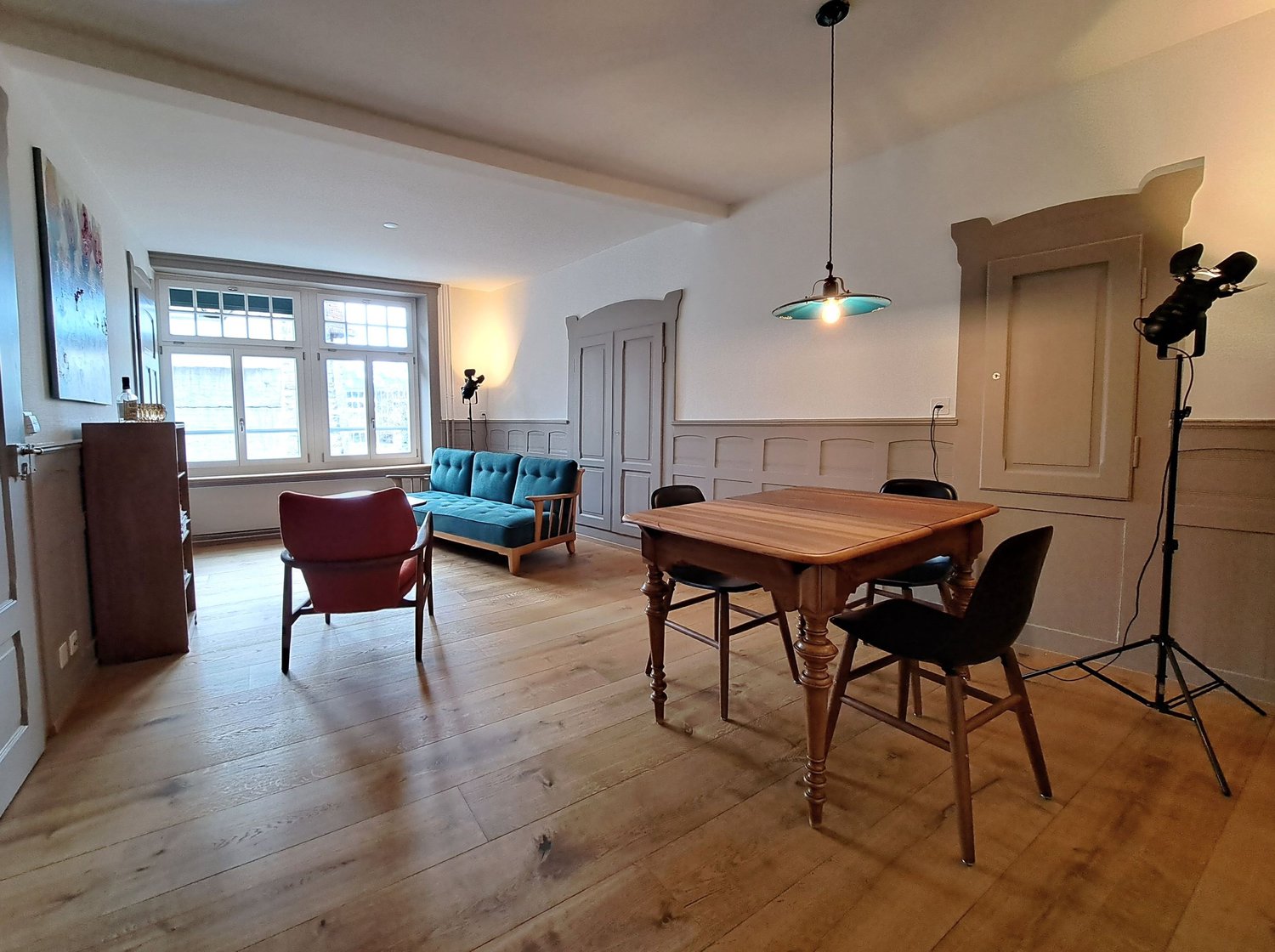 wooden floor, wooden table, blue sofa, red chair, wooden cabinet, lamp, tripod