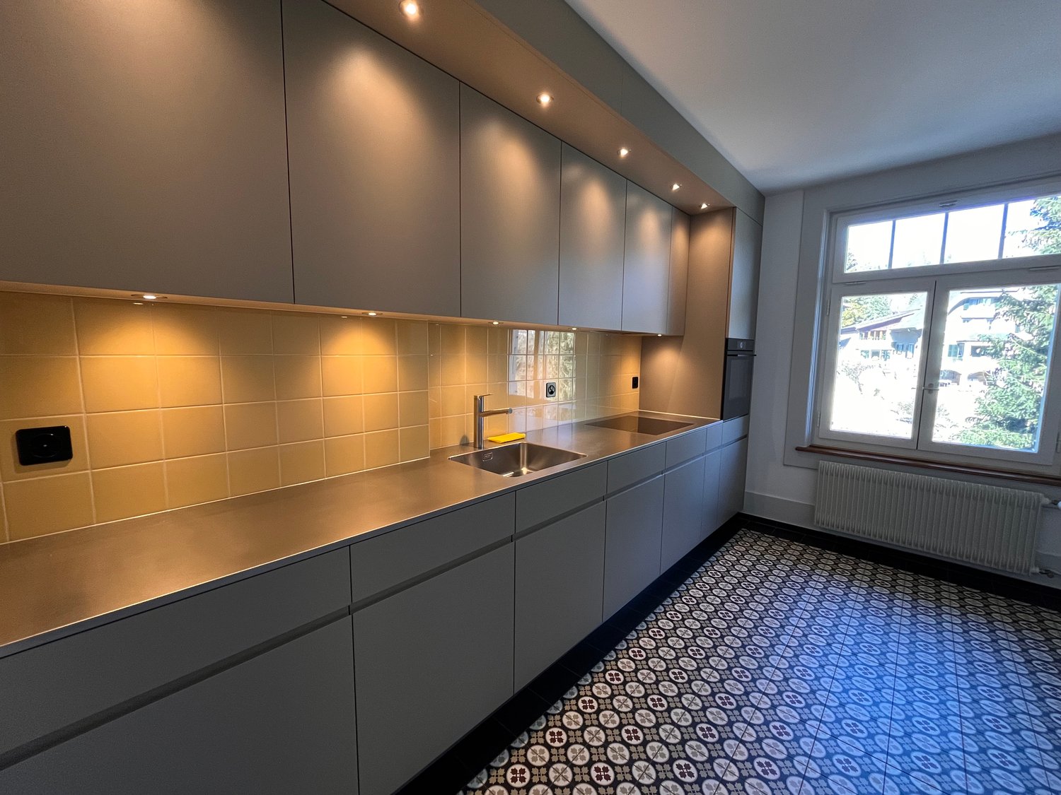 modern kitchen with stainless steel countertops, tiled backsplash, under-cabinet lighting, double sink, gas stove, and a window with a view