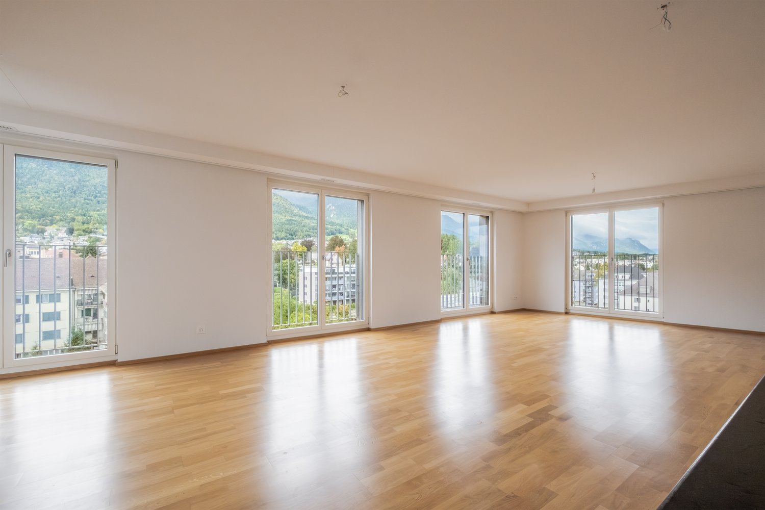 open room with glass walls, wooden floors, views of the mountains