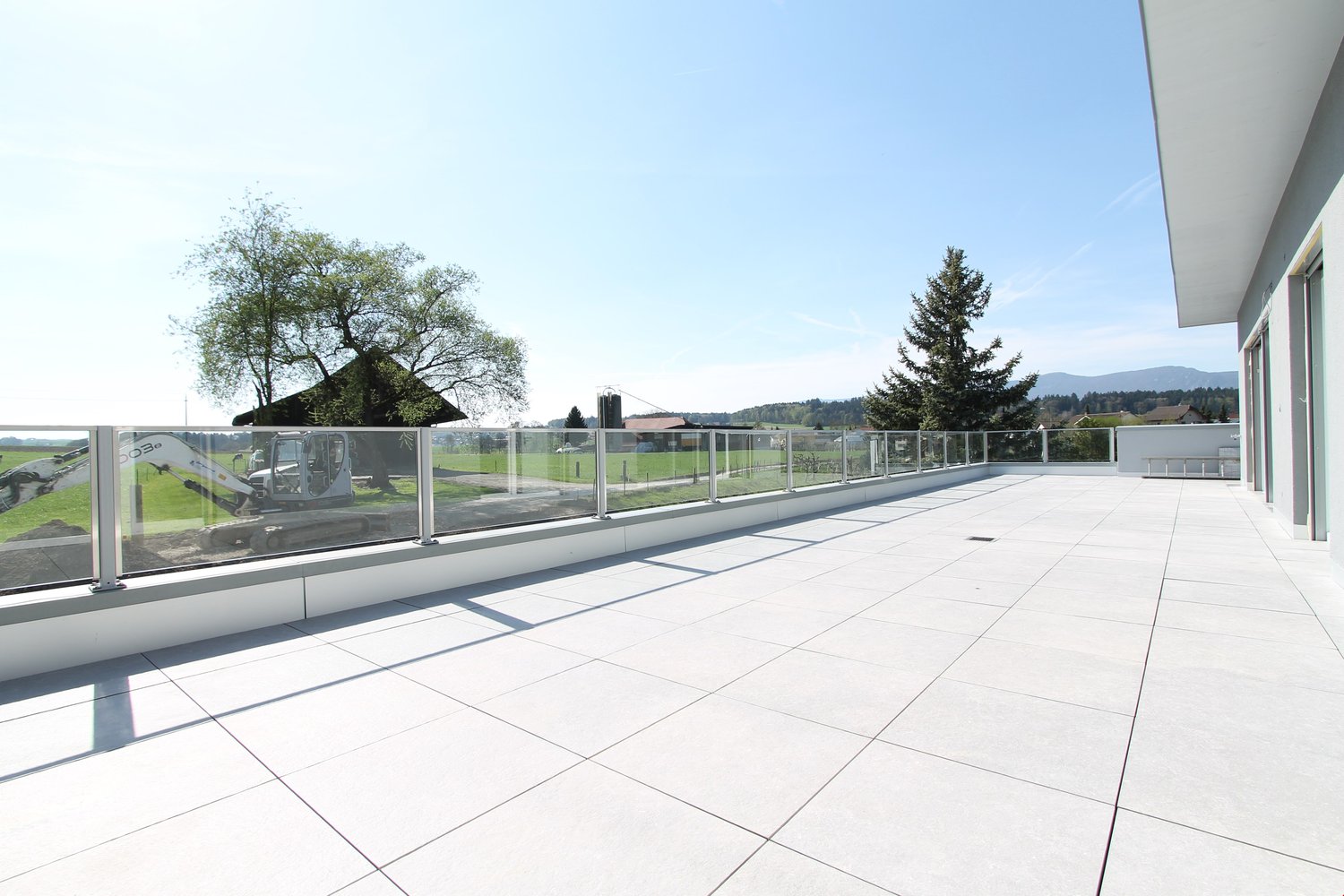 large balcony with glass railings, tiled floor, view of the surrounding landscape