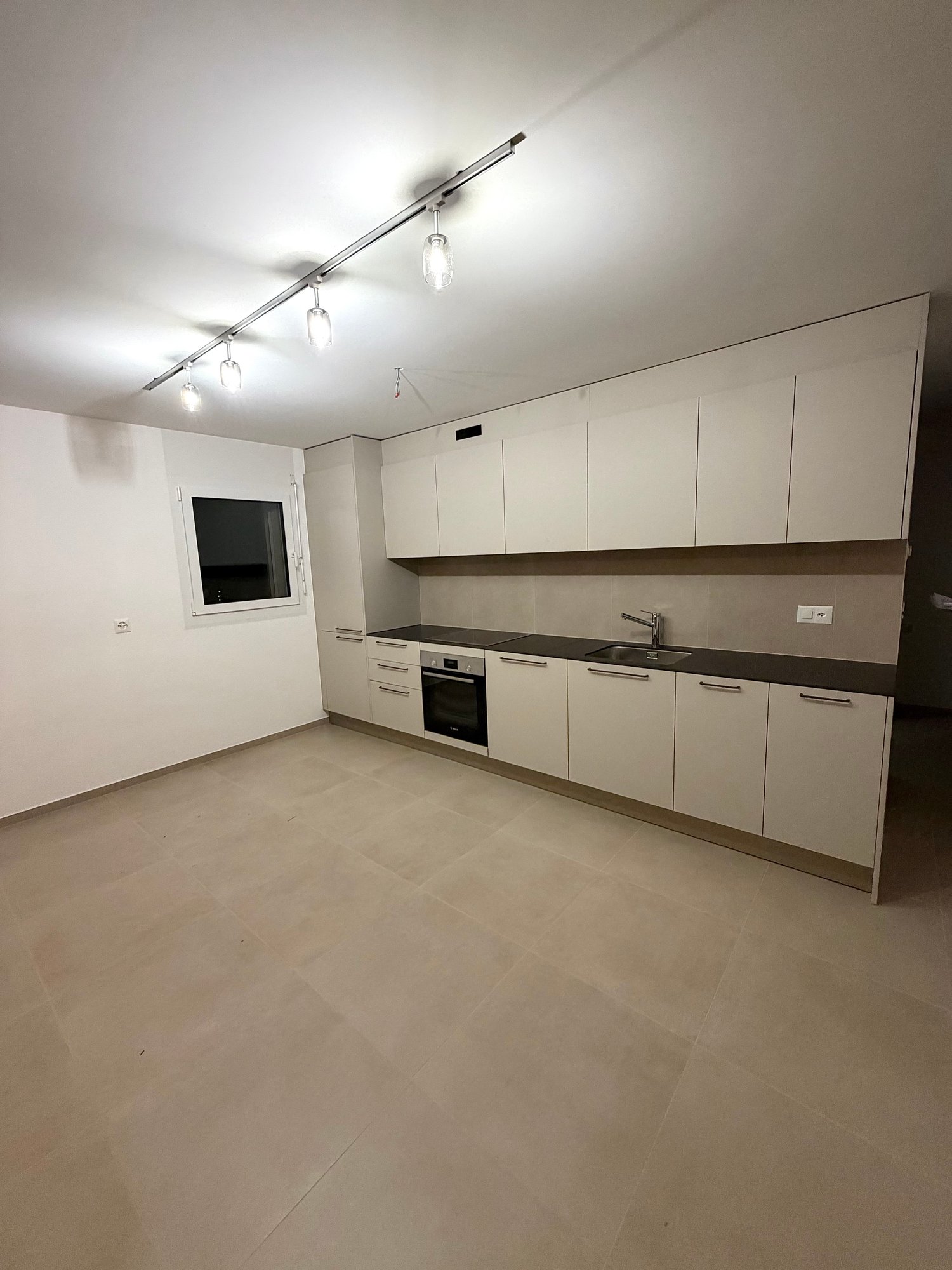 a kitchen with tile flooring, white walls, white cabinets, black countertops, built-in oven, stainless steel faucet, and a power outlet