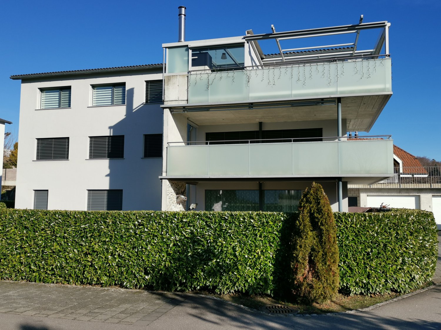 Three story house, white paint, green hedges, metal railing on balcony