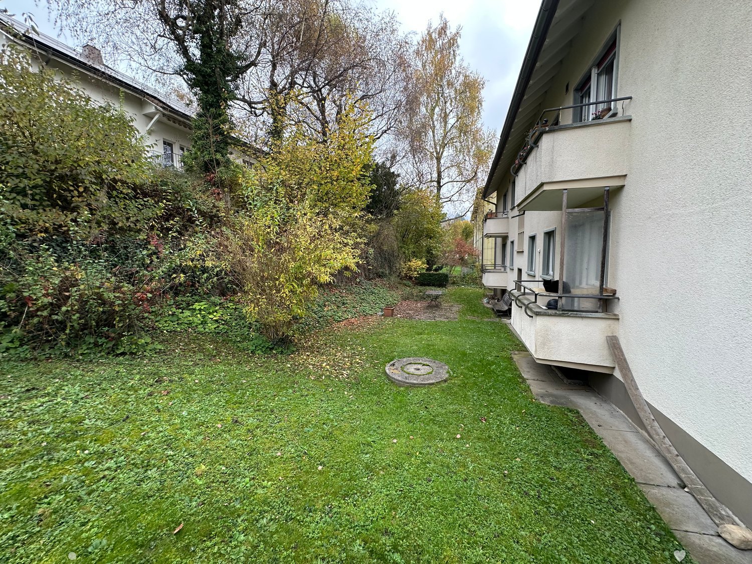 Garden with lawn, trees, bushes, balcony, paved area with table