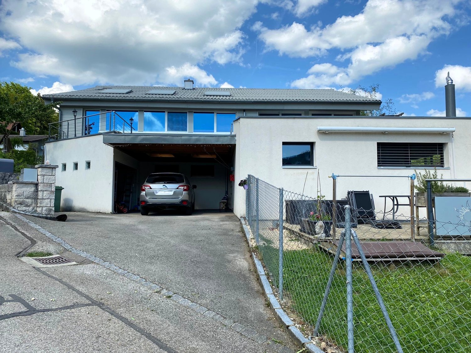 2-story modern house with a garage, large windows, and a fenced yard with outdoor furniture