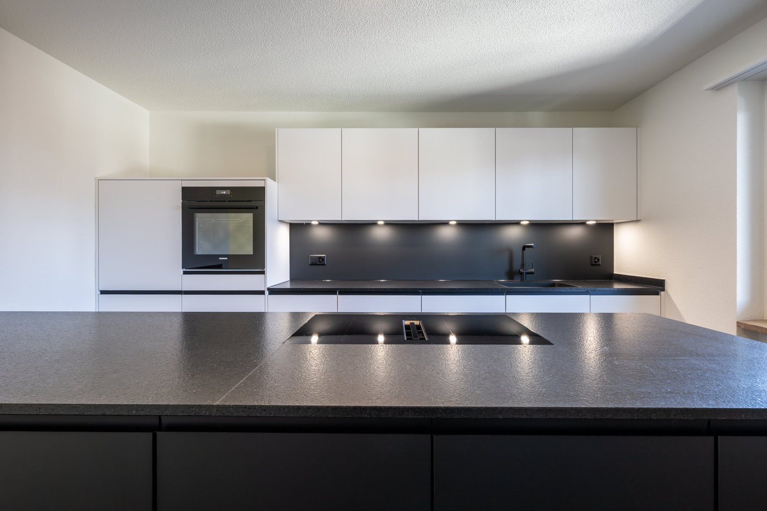 modern kitchen with white cabinets, black countertops, built-in oven, sink, faucet, induction cooktop
