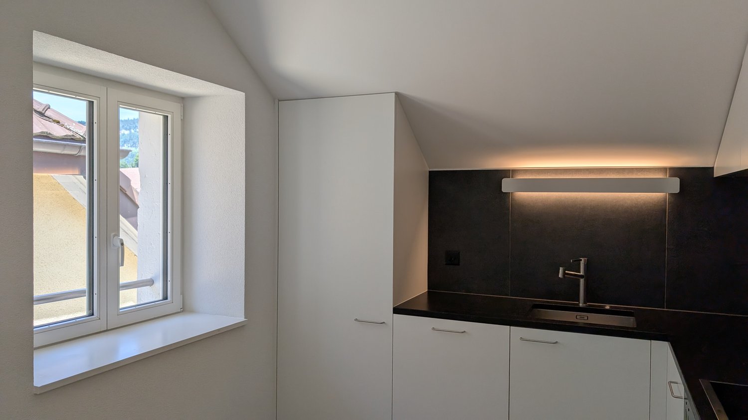 sleek white cabinets, black countertops, double sink with faucet, built-in lighting, a window with a white frame, small window ledge