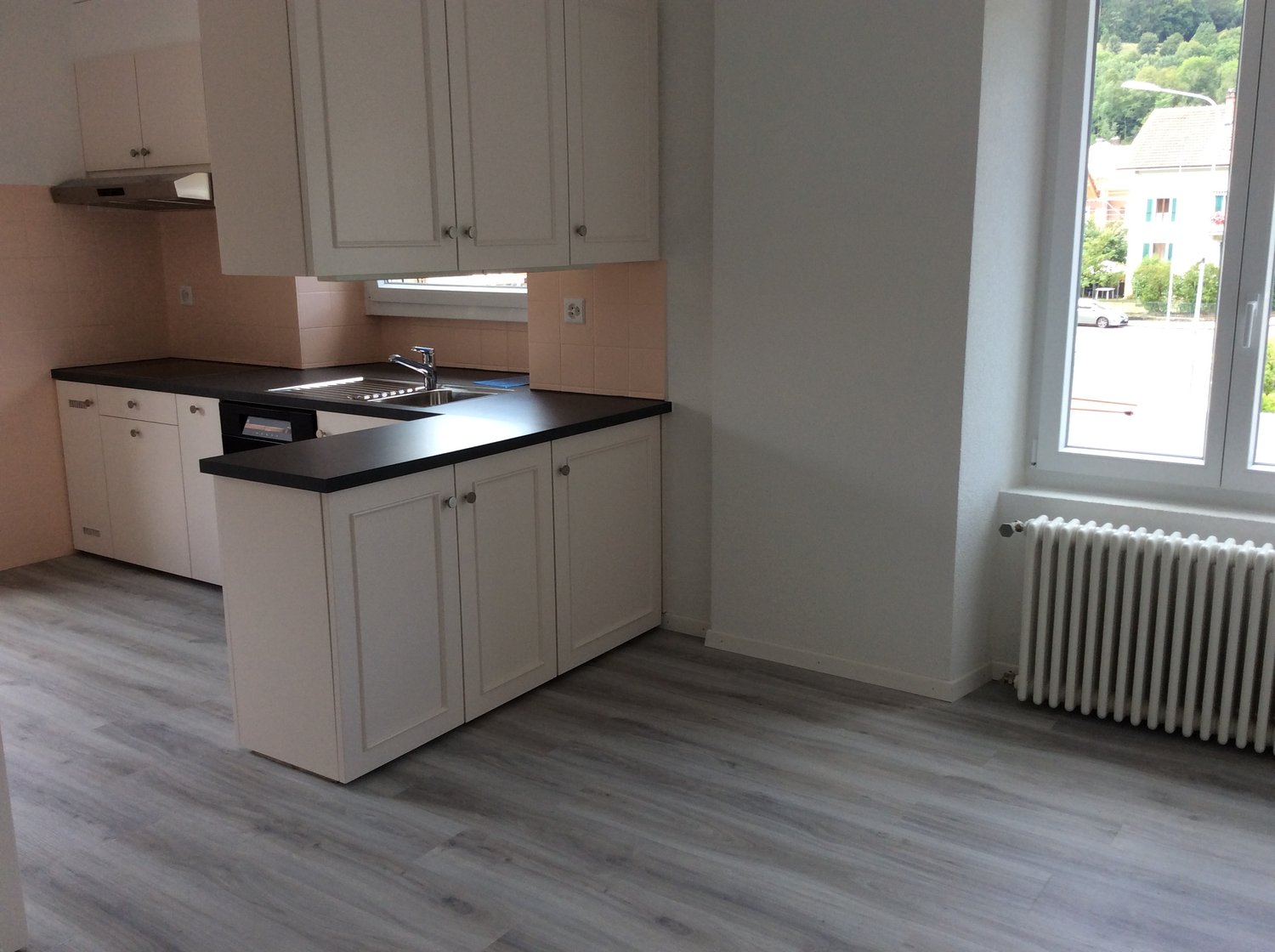 modern kitchen, white cabinets, black countertops, sink, faucet, under cabinet lighting, extractor hood, white floor, radiator