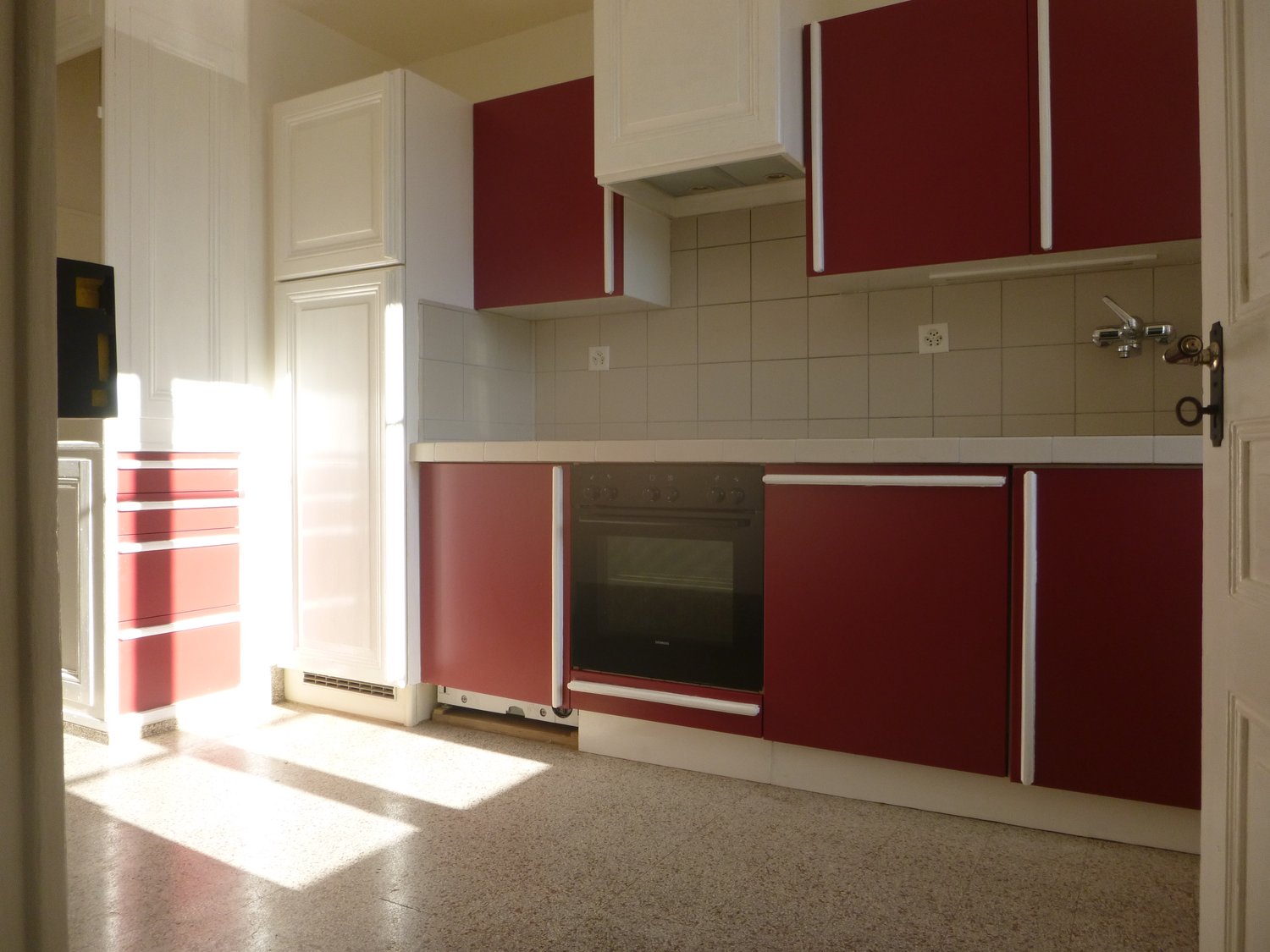 kitchen with modern red cabinets, gas oven, tiled walls, white refrigerator, extractor hood