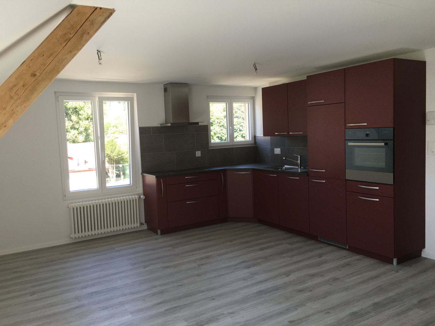 kitchen, maroon cabinets, gray tile backsplash, wooden floor, exhaust hood, stainless steel oven, white radiator