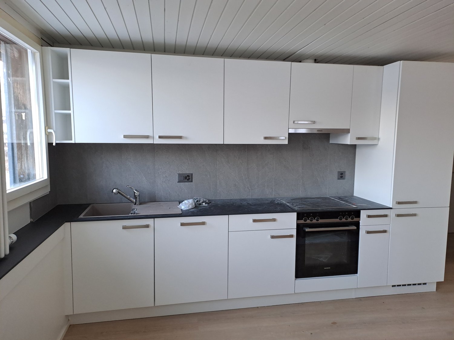 Modern kitchen with white cabinets, black countertops, stainless steel appliances, grey wall tiles, and wooden floor