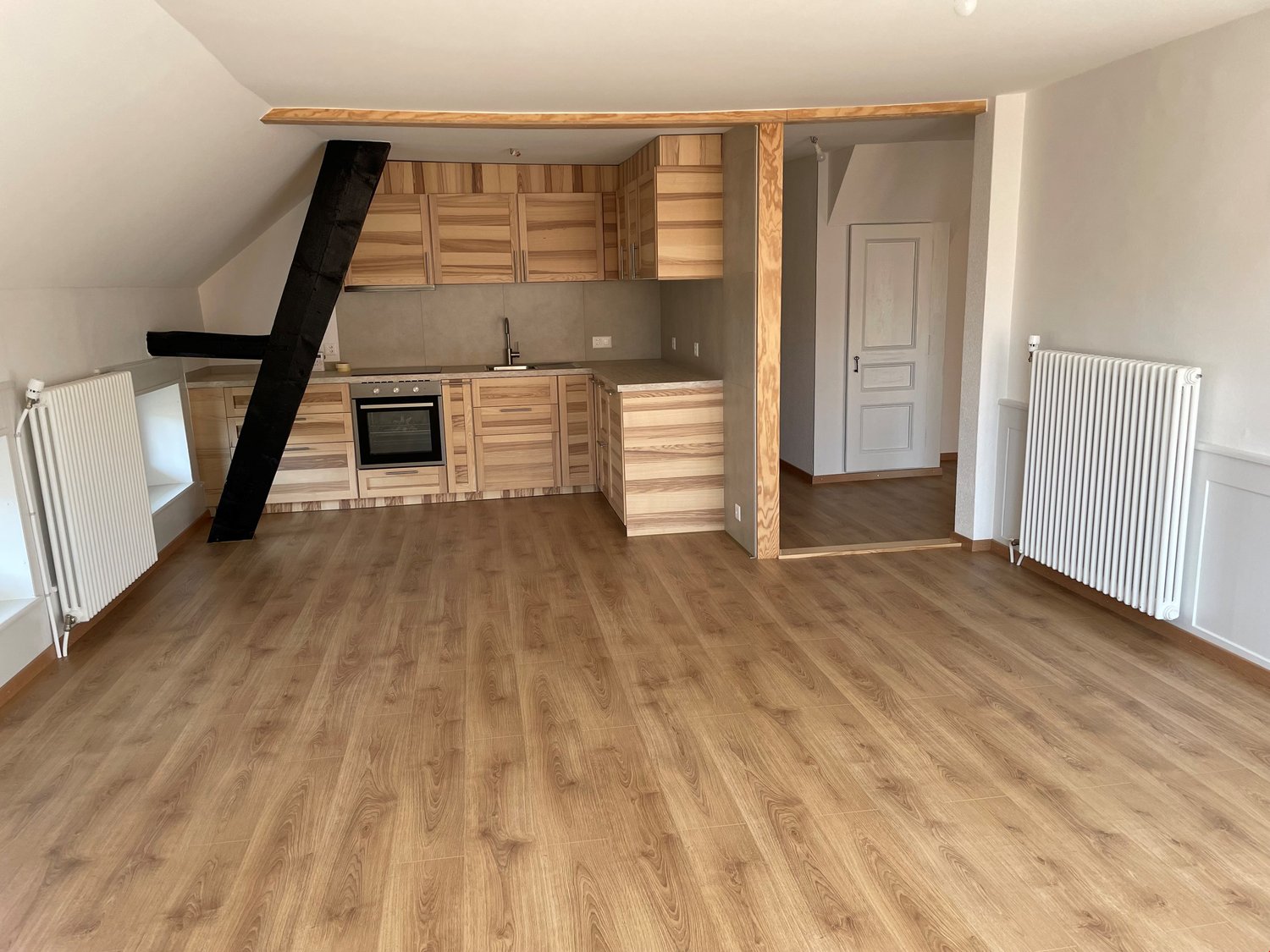 An empty kitchen area with wooden floor, wooden kitchen cabinets, integrated oven and extractor, gas stove, and white radiators on both sides