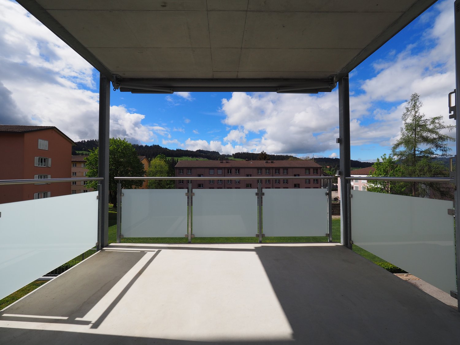 Balcony with railings, glass walls, concrete floor, and green grass area