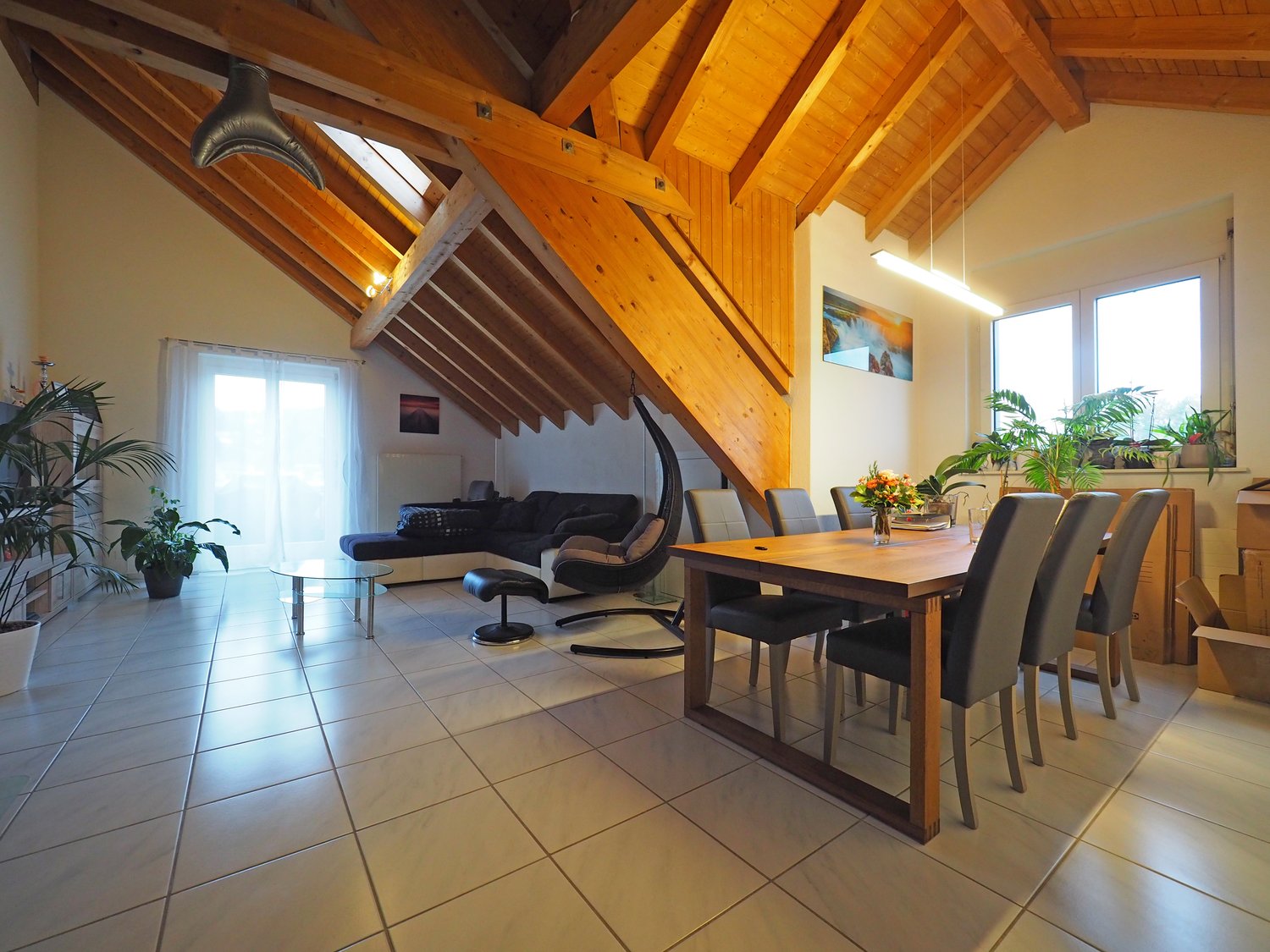 dining area with a wooden table and 6 chairs, flowers on the table, exposed wooden beams, black sofa, wooden floor