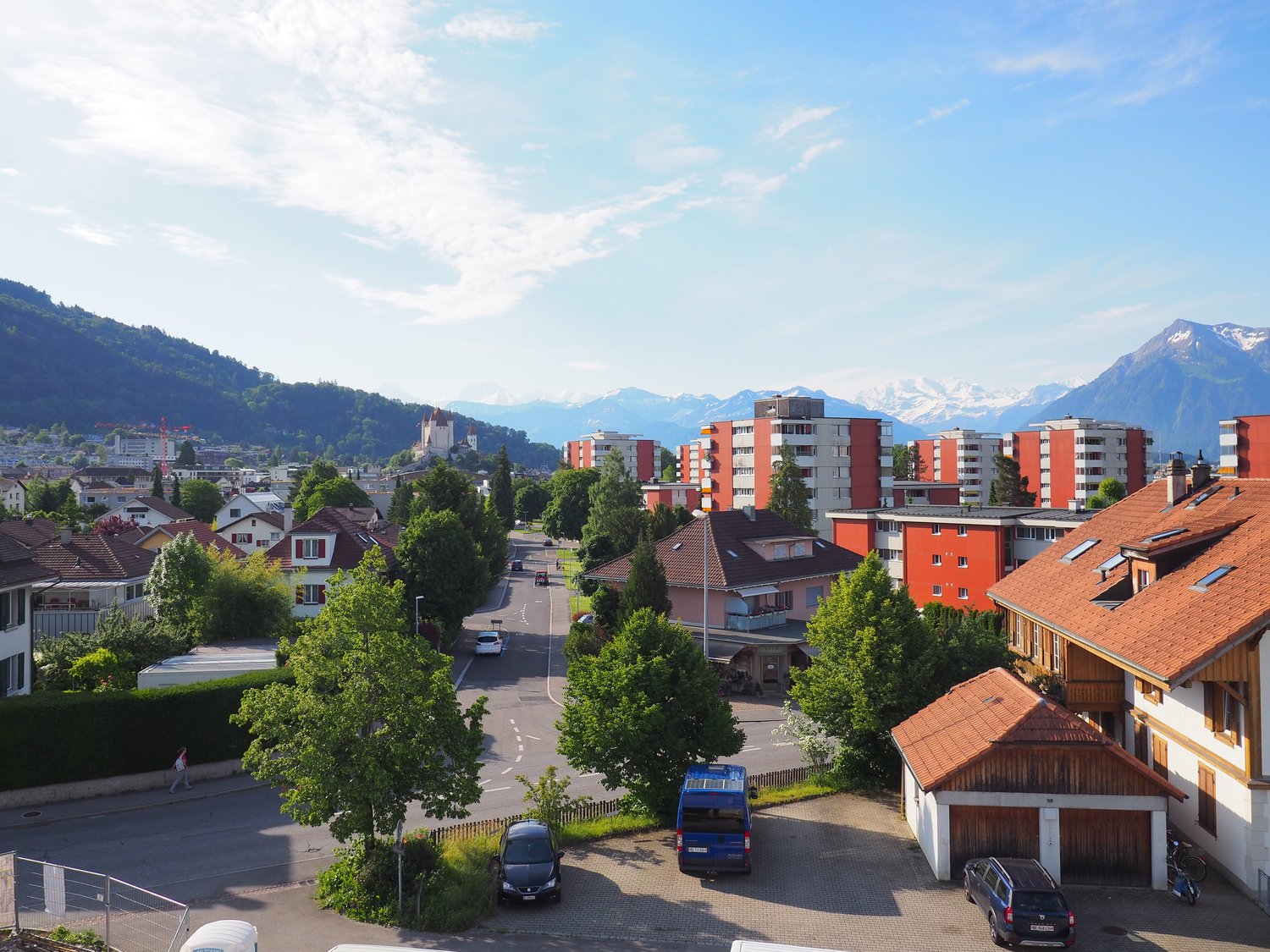 city view, various houses and buildings, mountain view, several cars parked
