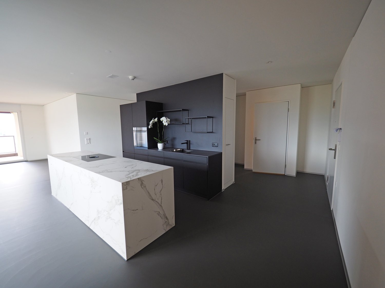 modern kitchen with marble countertop, black cabinets, stainless steel appliances, white walls, gray flooring