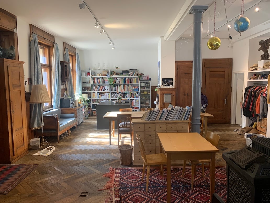 bright room with large windows, wooden shelves, bookshelves, wooden flooring, desk, chairs, cabinets, and decorative items