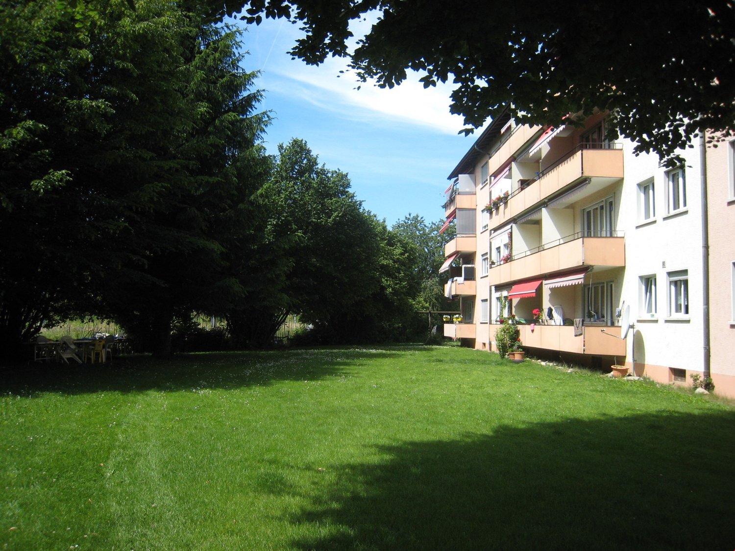 Multi-story residential building, green lawn, trees, balconies, windows, potted plants