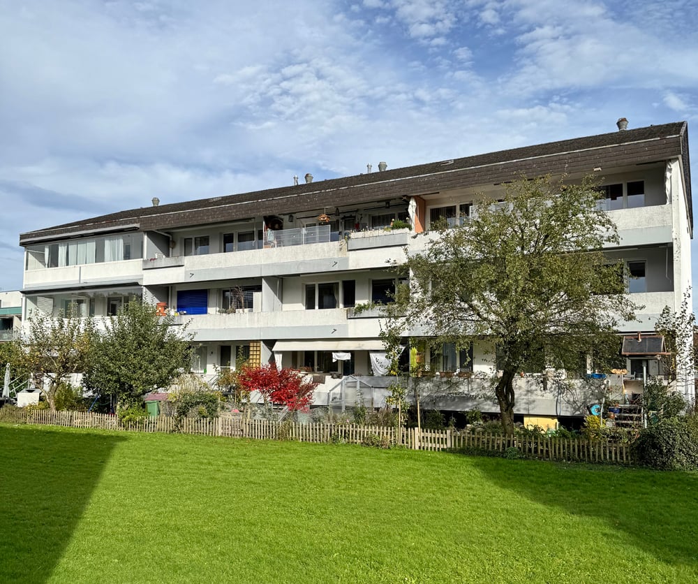 White apartment building with balconies, located on a hill, large grassy area in front